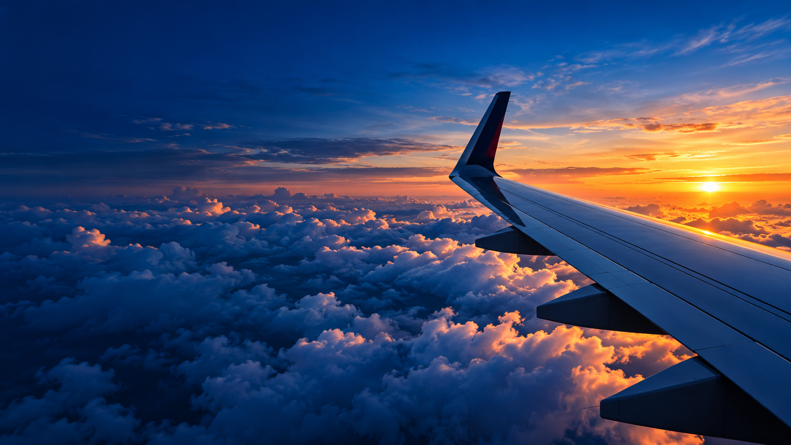 Commercial passenger jet airliner wing flying above clouds at sunset